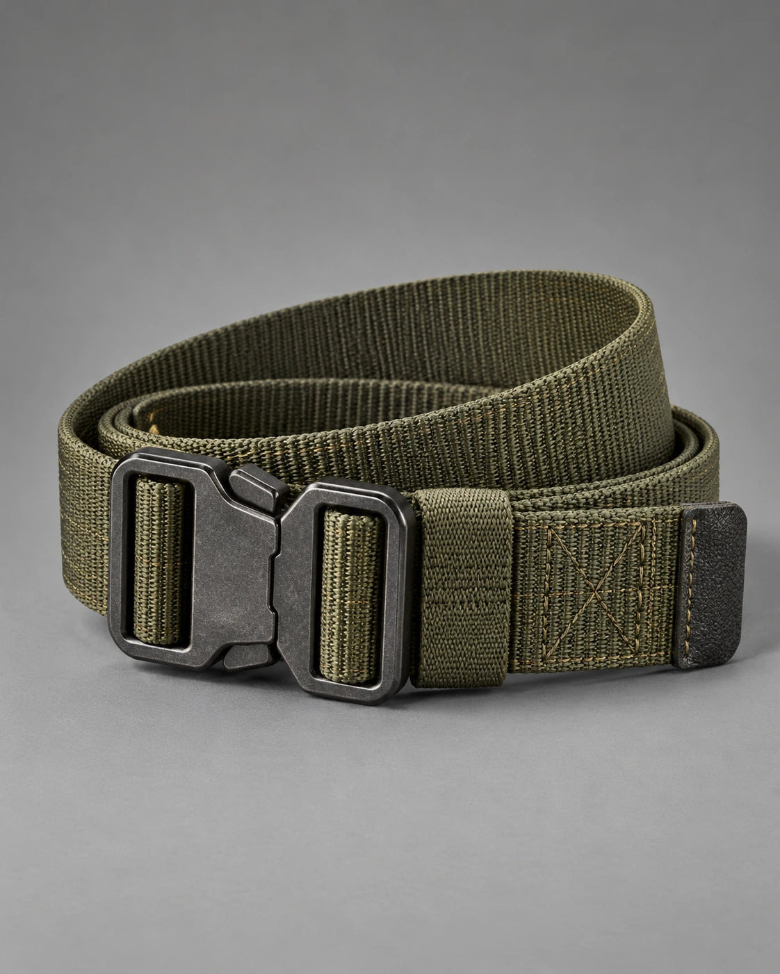 Olive webbing utility belt coiled with its dark metal buckle visible on a grey studio surface.