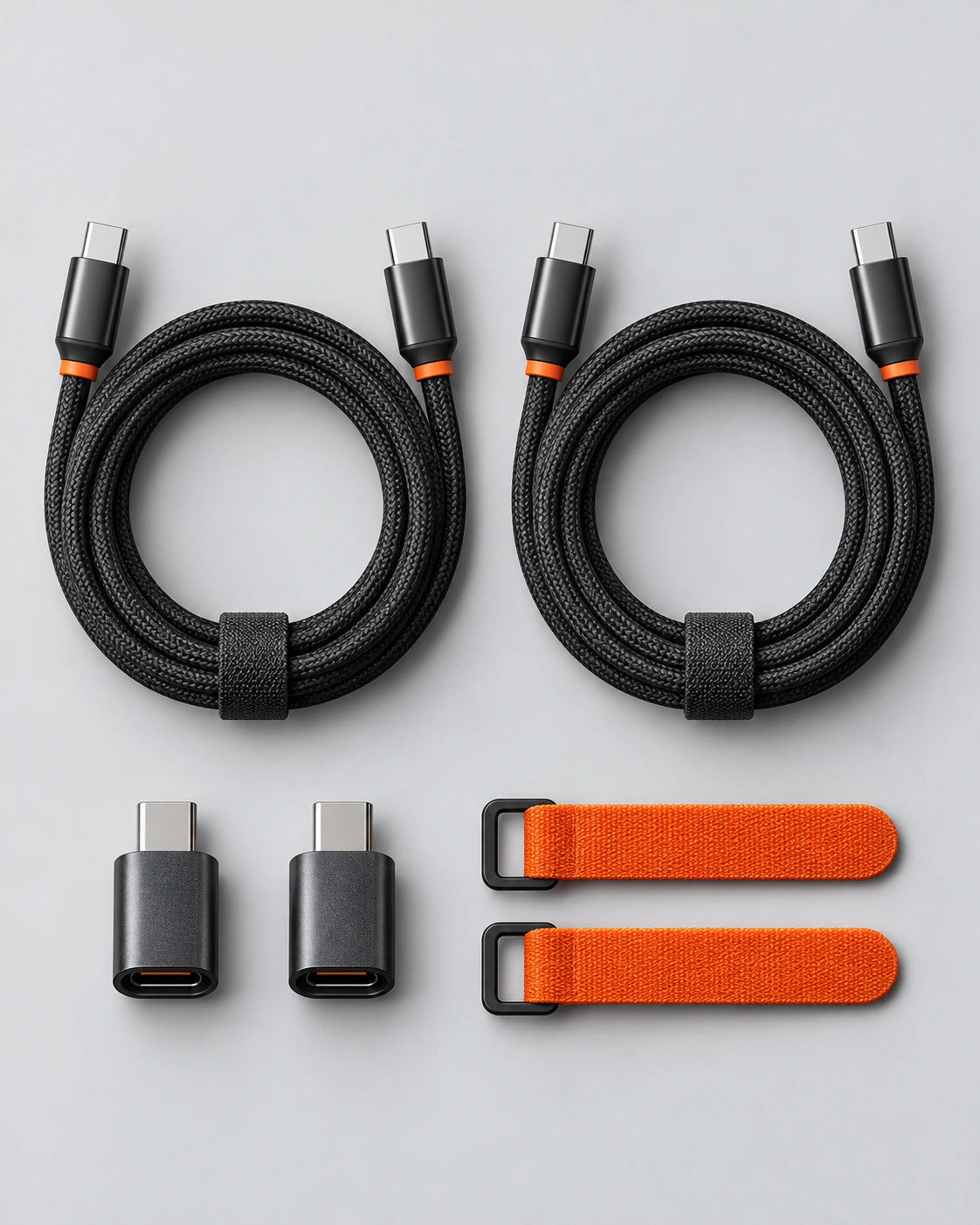 Two coiled black braided cables, two compact adapters and orange cable ties arranged on a grey surface.