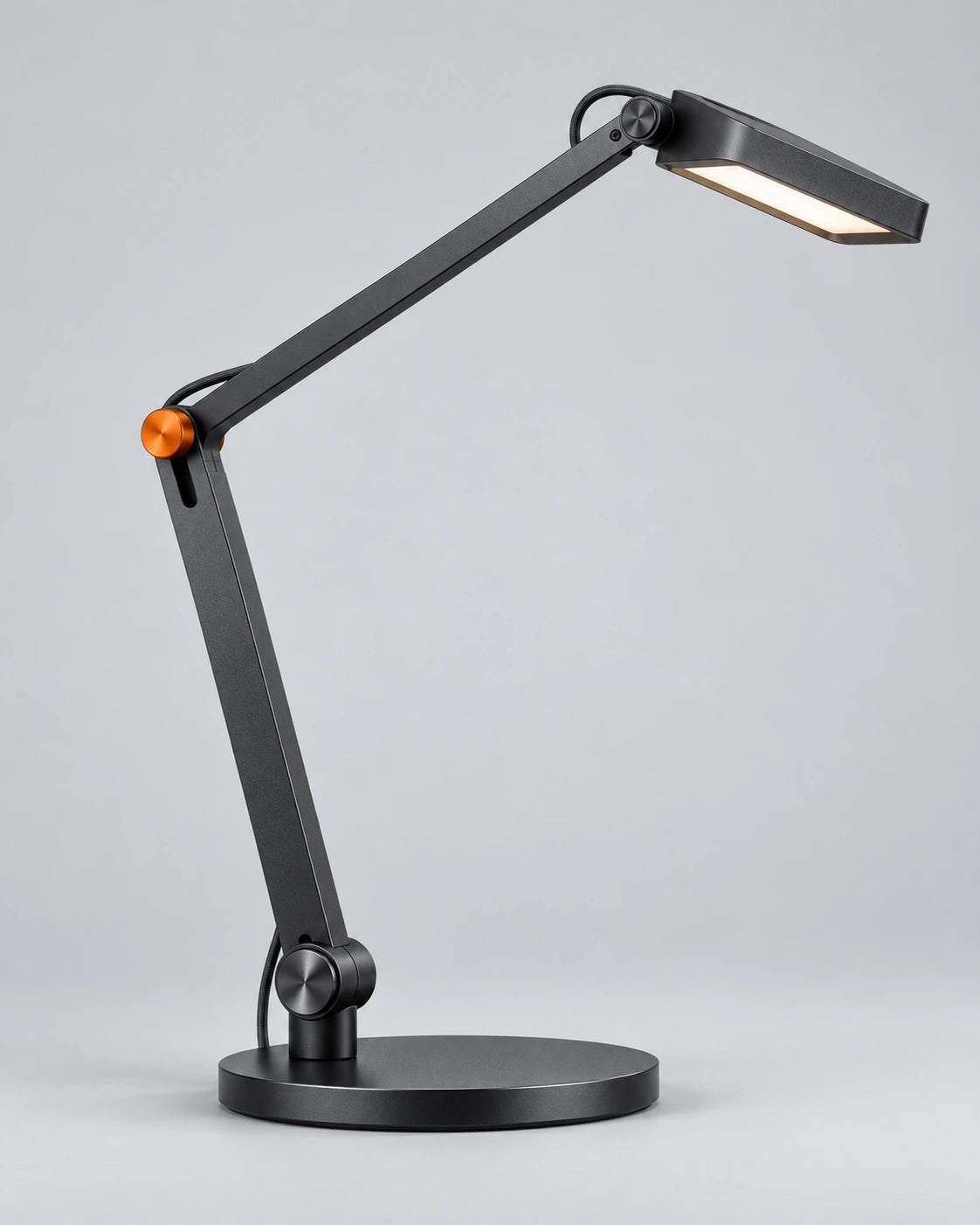 Graphite articulated desk lamp with a slim base and an orange joint detail on a light-grey background.