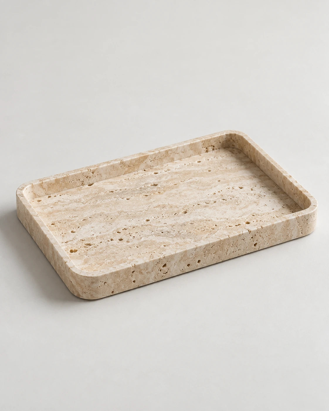 Pale travertine-style stone tray with rounded corners and a raised edge on a light studio surface.