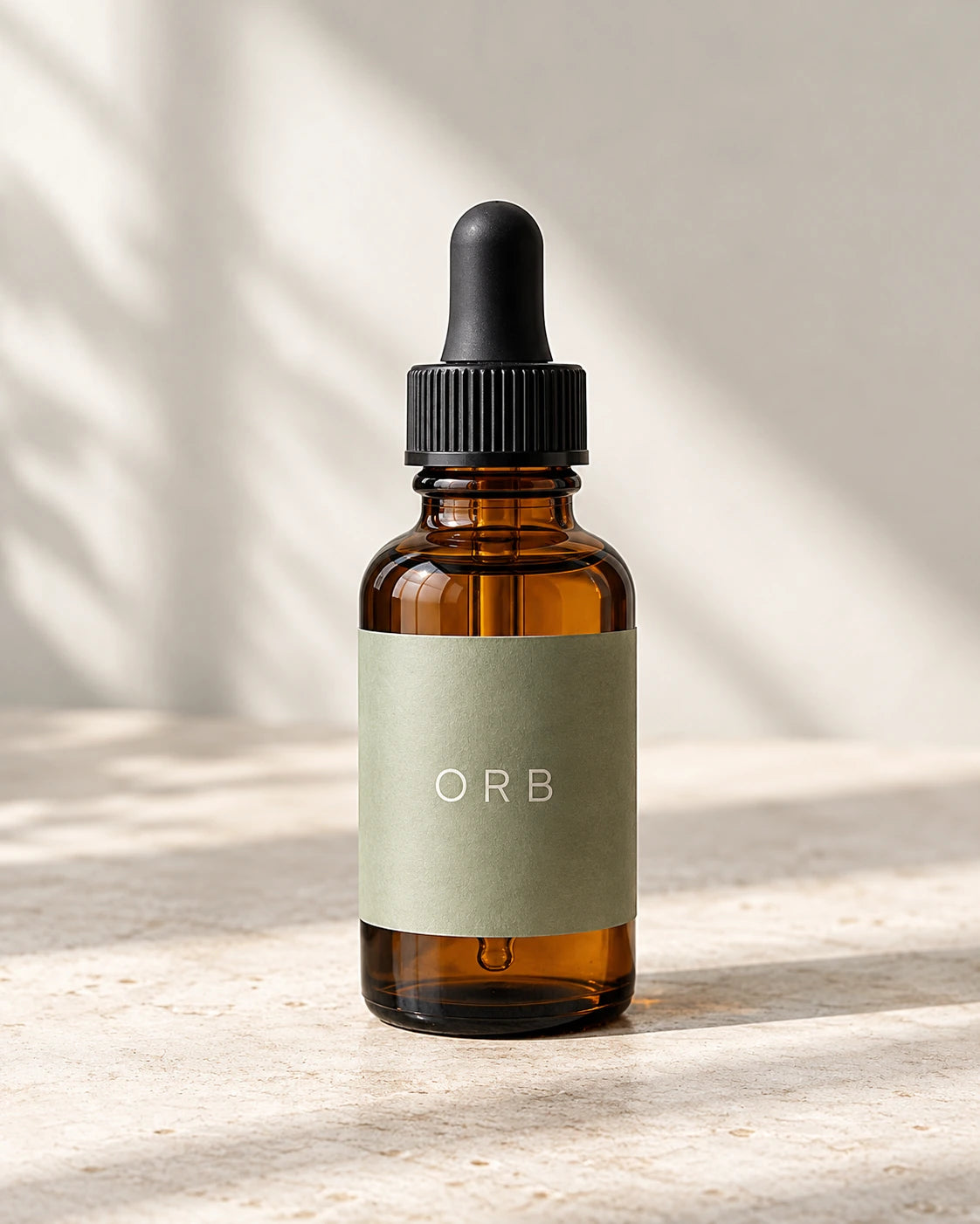 Small amber glass aromatic-oil bottle with a sage label and black dropper on a pale studio surface.