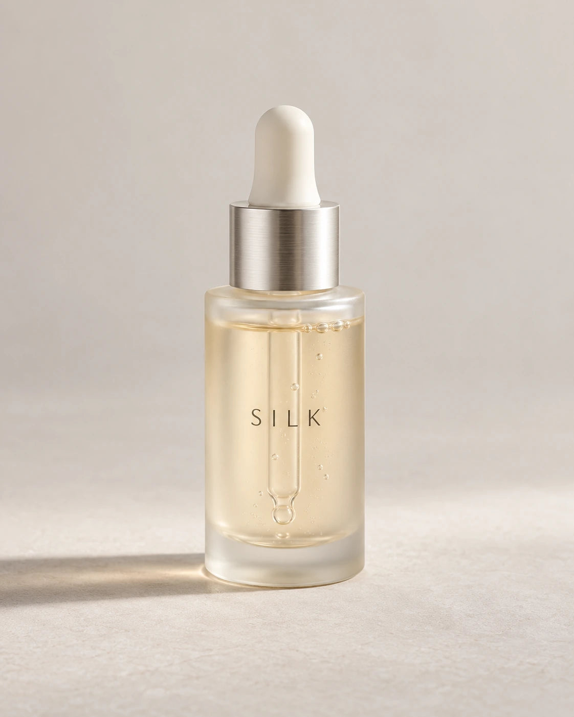 Clear glass serum bottle with an ivory dropper and pale liquid, photographed on a light studio background.