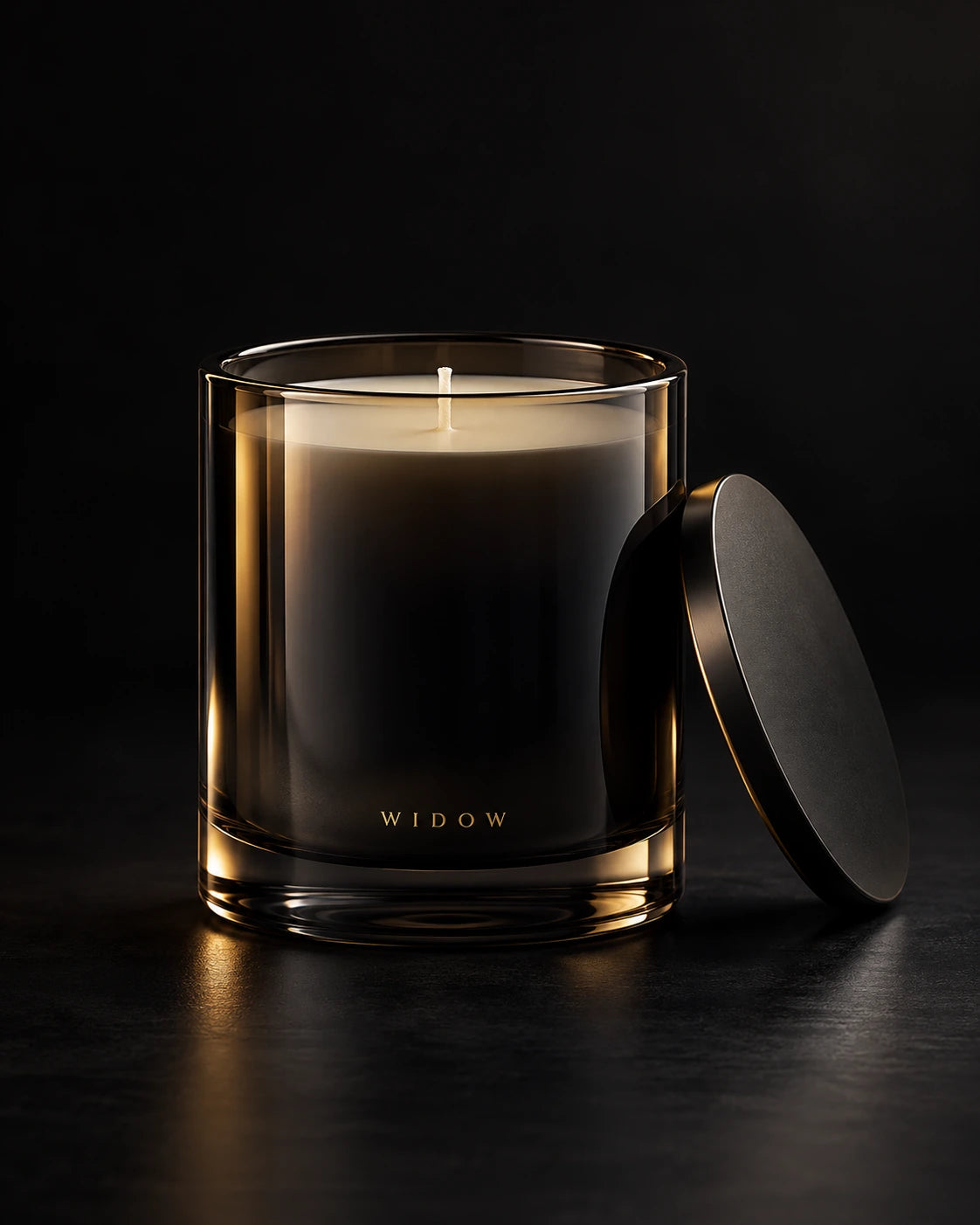 Smoked black glass candle with a single wick and matching lid on a dark studio surface.