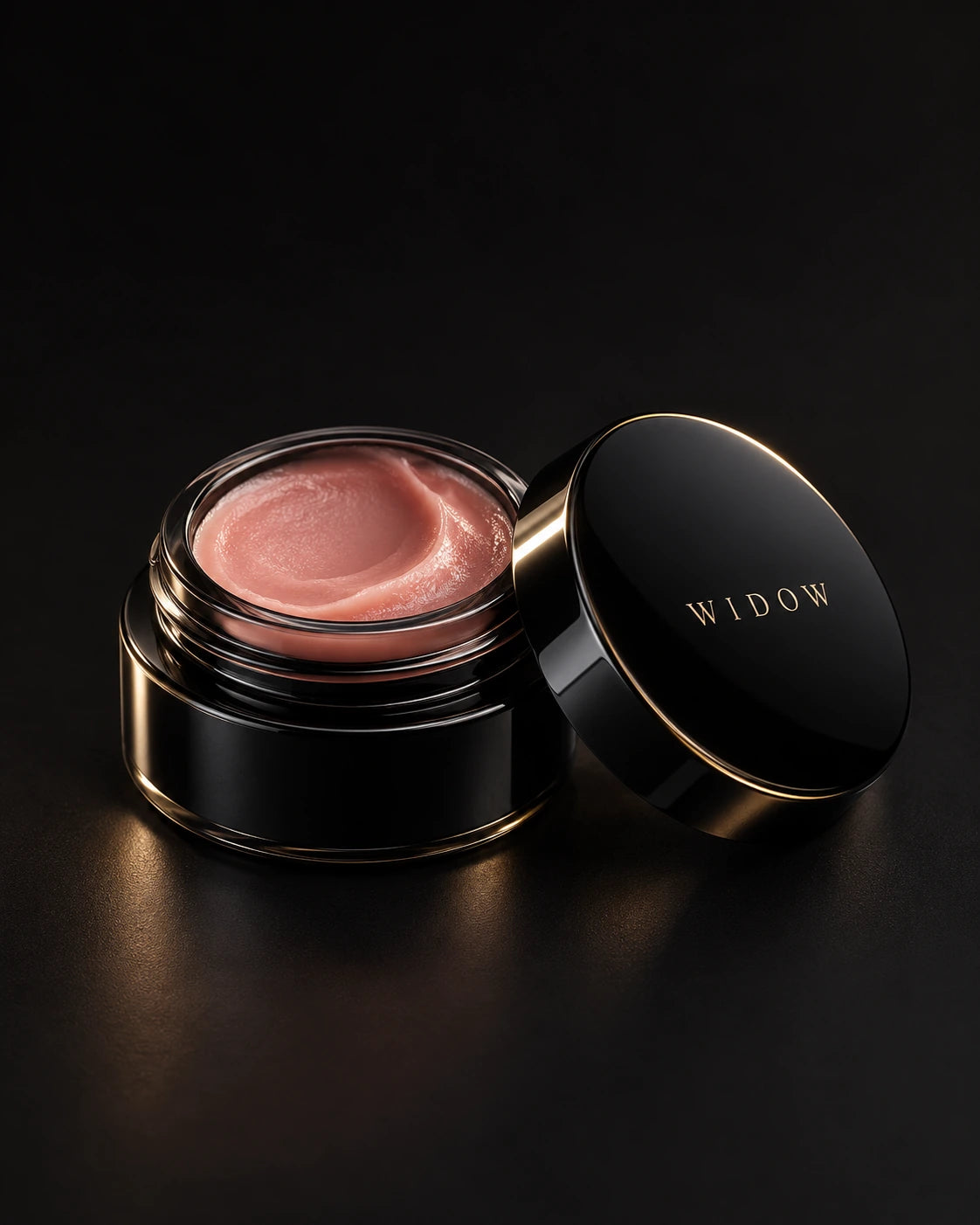 Open black cosmetic jar containing rose-tinted balm, with its polished lid beside it on a dark backdrop.